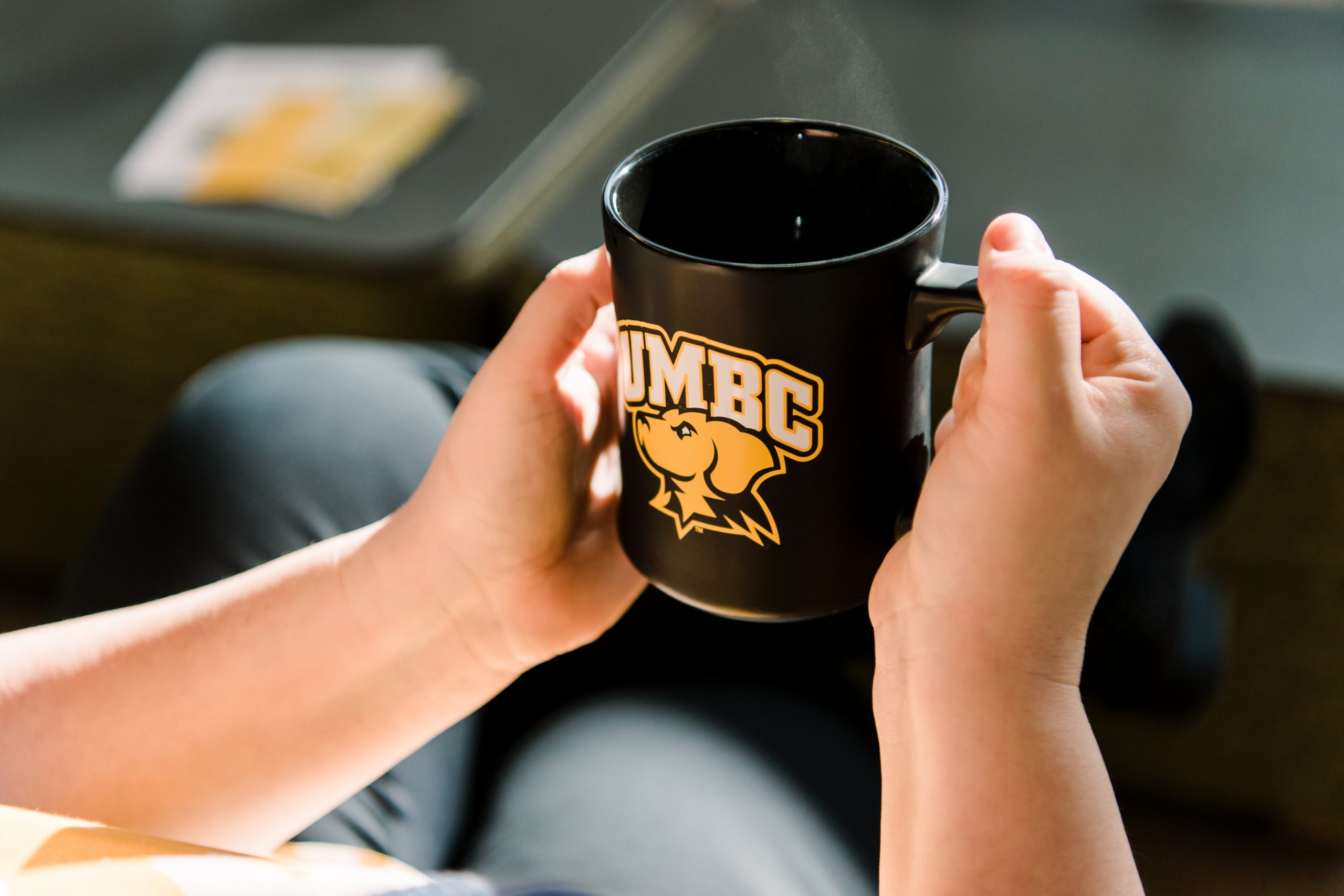 Hands holding a steaming UMBC mug