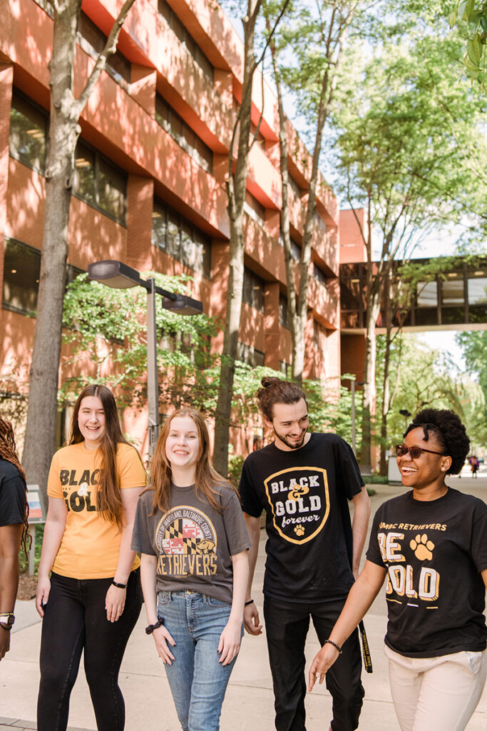 A diverse group of students wearing UMBC black and gold spirit t-shirts, walking together on academic row.